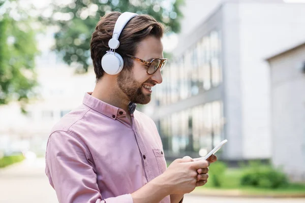 スマートフォンやヘッドフォンを屋外で使用してシャツに笑みを浮かべてビジネスマンの側面図 — ストック写真