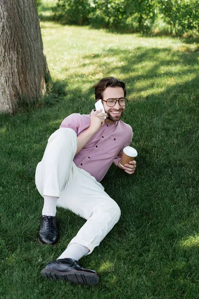 若いビジネスマンが携帯電話で話してコーヒーを持って草の上に行く — ストック写真