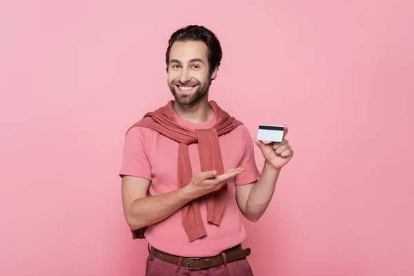 Pozytywny Człowiek Wskazując Kartę Kredytową Stojąc Samotnie Różowym — Zdjęcie stockowe