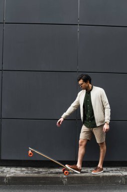 Güneş gözlüklü ve bombacı ceketli genç adam binanın yakınında uzun bir sörf tahtası kullanıyor. 
