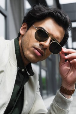 stylish young man adjusting trendy sunglasses outside clipart
