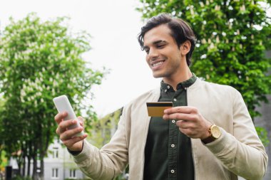 Mutlu adam kredi kartı tutarken akıllı telefon kullanıyor.