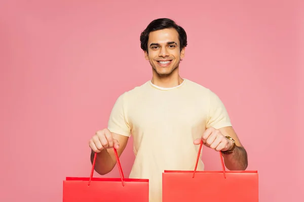 幸せな若い男はピンクに隔離された赤いショッピングバッグを保持 — ストック写真