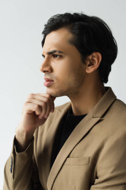 Şık bej ceketli düşünceli genç adam Gri üzerine izole edilmiş bir şekilde yüzünü çeviriyor.