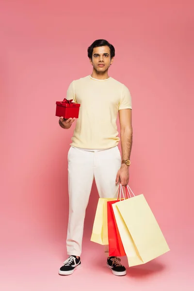 Полная Длина Молодого Человека Держащего Красную Подарочную Коробку Пакеты Покупок — стоковое фото