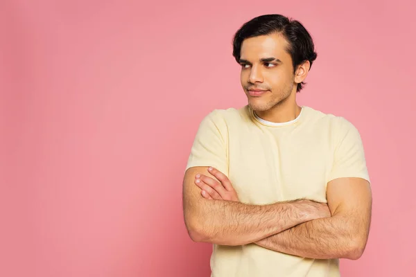 dissatisfied young man with crossed arms looking away isolated on pink