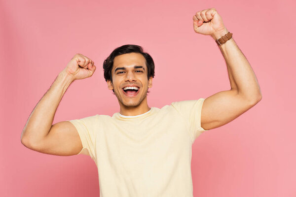 excited young man with raised hands isolated on pink