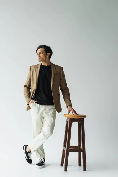 Joven Elegante Chaqueta Beige Posando Con Mano Bolsillo Cerca Silla — Foto de Stock