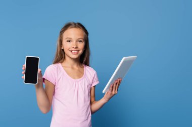 Dijital tablet tutan ve mavi üzerinde akıllı telefonu gösteren çocuk. 