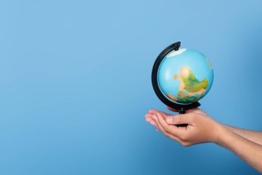 Cropped view of schoolkid holding globe on hands isolated on blue  clipart