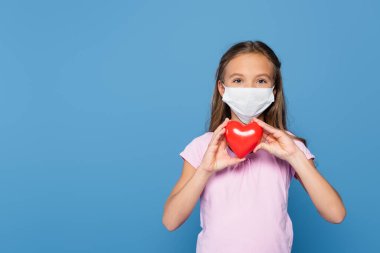 Kırmızı kalbi mavi renkte tutan tıbbi maskeli çocuk. 