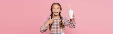 Neşeli çocuk jest yapıyor ve elinde pembe pankartta izole edilmiş milkshake tutuyor. 