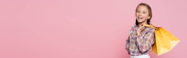 Sarı çantalı heyecanlı çocuk pembe pankartta izole edilmiş kameraya gülümsüyor.