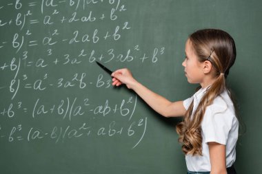 preteen schoolgirl pointing with pen at mathematic equations on chalkboard clipart