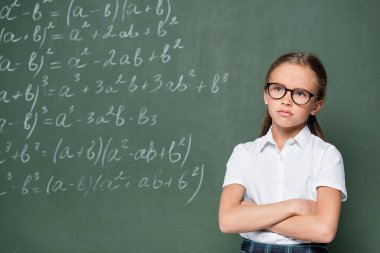 offended schoolgirl standing with crossed arms near chalkboard with equations clipart