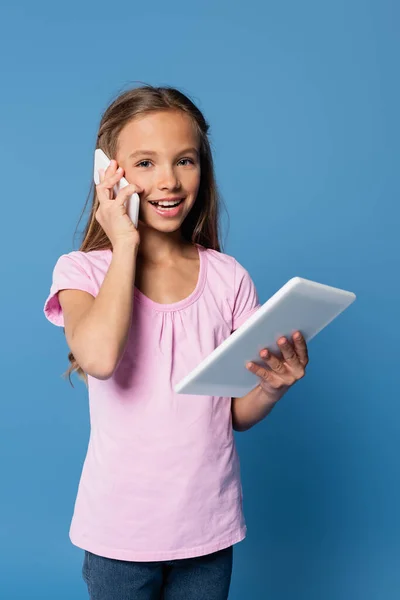 Pozitivní Dívka Mluví Smartphone Drží Digitální Tablet Izolované Modré — Stock fotografie