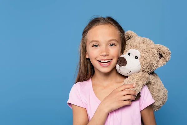 Kid with soft toy smiling at camera isolated on blue