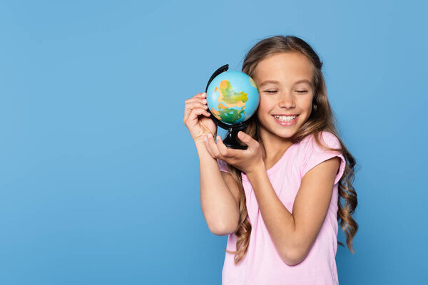 Girl with closed eyes smiling while holding globe isolated on blue 