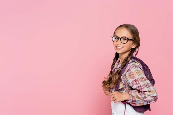 穿着眼镜和背包的未成年女学生对着用粉色隔离的相机笑着 — 图库照片
