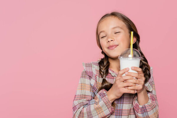 Pleased preteen girl with closed eyes holding milkshake isolated on pink 