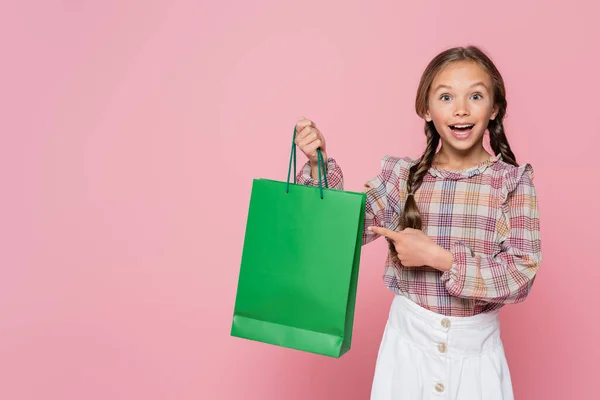 Изумленный Счастливый Ребенок Указывая Зеленый Торговый Мешок Изолирован Розовый — стоковое фото