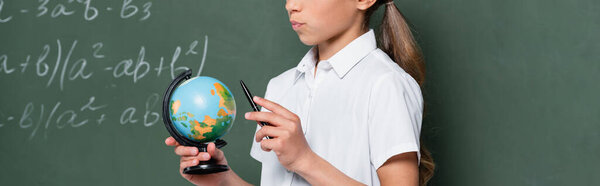 cropped view of schoolkid with small globe and pen near chalkboard, banner