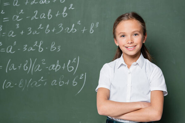 школьник со скрещенными руками, улыбающийся в камеру рядом с уравнениями на доске