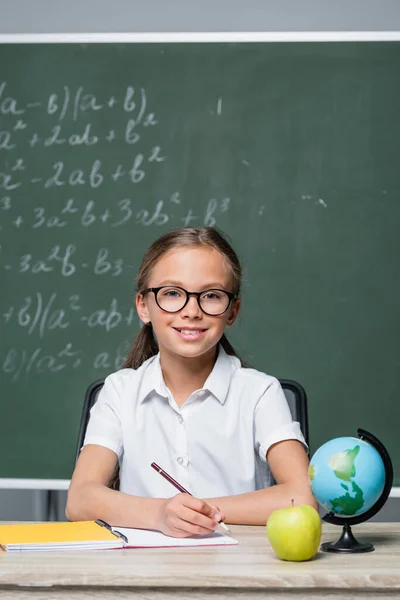 Positive Schoolgirl Pen Smiling Camera Globe Notebook Desk — Stock Photo, Image