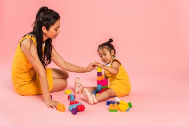 Asyalı kadın ve kız pembe üzerinde oturuyor ve yapı taşı oynuyorlar. 