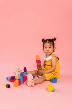 Asyalı bebek elbiseli çocuk pembede yapı taşı oynuyor. 