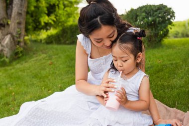 Asyalı çocuk parkta annesinin yanında samandan lezzetli bir milkshake içiyor.