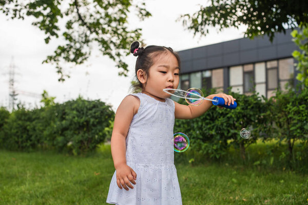 asian girl in dress blowing in bubble stick outside