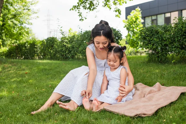 Young Asian Mother Touching Feet Toddler Daughter Sitting Picnic Blanket — Stock Photo, Image