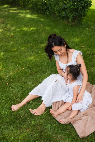 ピクニック毛布の上に座っているドレスを着たアジア系の母親と娘の高い角度の眺め — ストック写真