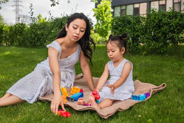 アジア系の母親と幼児の女の子が公園でピクニック毛布の上でブロックを演奏 — ストック写真