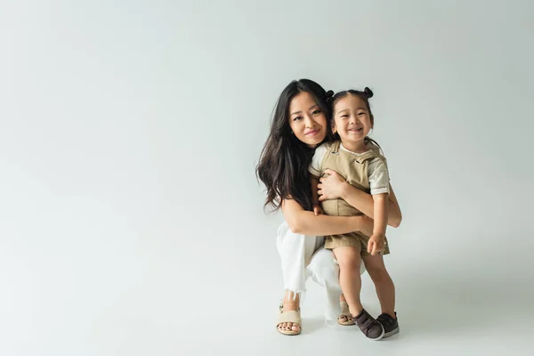 Full Length Stylish Asian Mother Hugging Toddler Daughter Grey — Stock Photo, Image