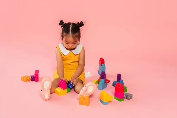 穿着黄色衣服的亚洲幼儿女孩在粉红上玩积木游戏 — 图库照片