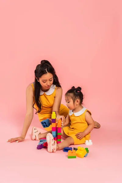黑发亚洲女人和女儿坐在粉红上玩积木游戏 — 图库照片