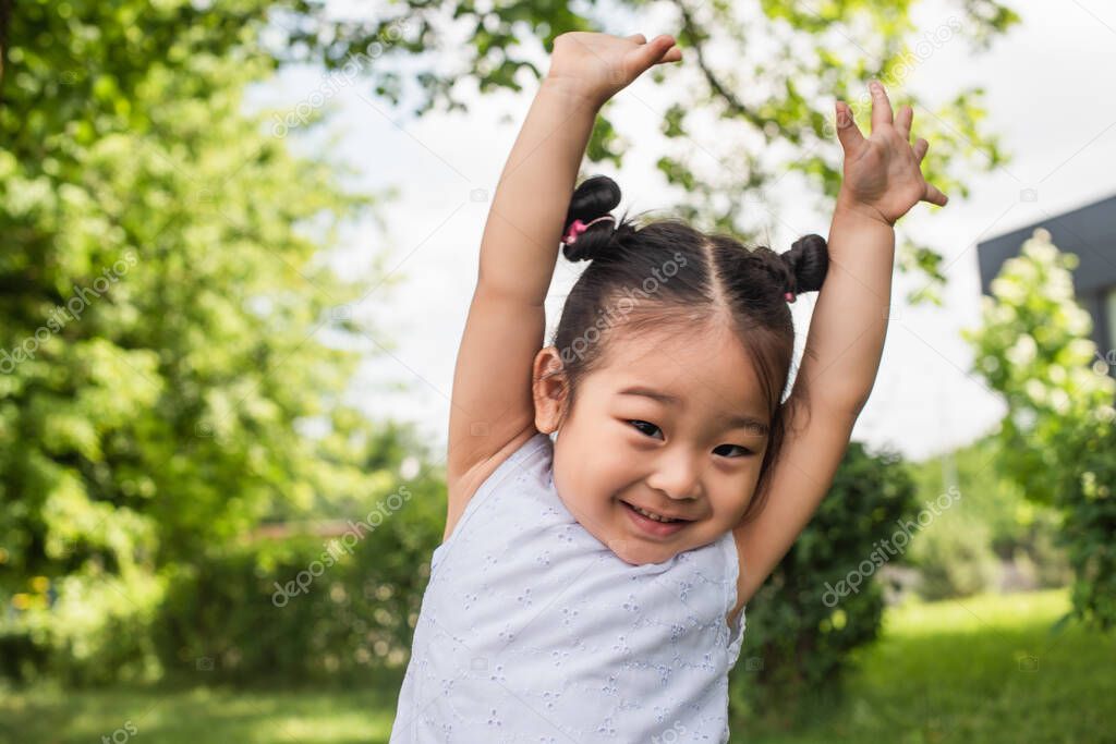 playful asian kid standing with raised hands and smiling outside