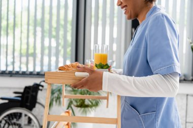 Afro-Amerikan hemşirenin elinde tepsiyle klinikte yemek tutarken görüntüsü. 