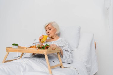 Hastanede yatağın yanında portakal suyu içen yaşlı bir kadın. 