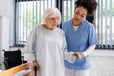 Klinikte bastonlu bir hastanın elini tutan Afrikalı Amerikalı hemşire. 