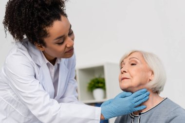 African american docktor in while coat checking neck of elderly patient  clipart