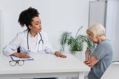 African american doctor looking at elderly patient touching arm  clipart