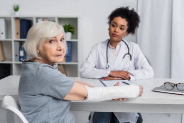 Kolunda bandaj olan son sınıf öğrencisi Afro-Amerikan doktorunun yakınındaki kameraya bakıyor. 