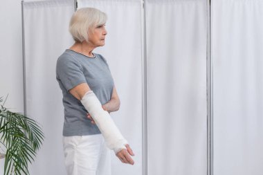 Klinikte kırık kolunda yara bandı olan yaşlı bir hastanın yan görüntüsü. 