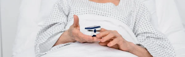診療所のベッドで酸素濃度計を保持する高齢患者の作物ビュー バナー — ストック写真