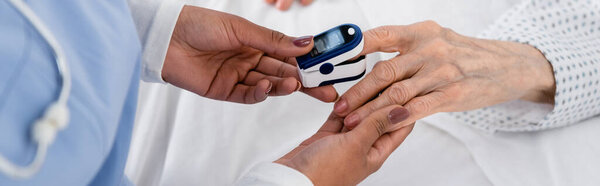 Cropped view of african american nurse fastening digital oximeter on hand of elderly patient, banner 