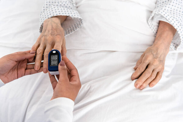 Top view of african american nurse fastening oximeter on hand of senior patient 