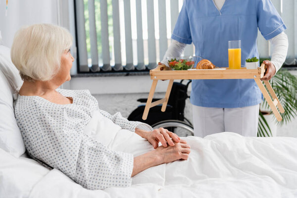 African american nurse holding food on tray near elderly patient in hospital ward 